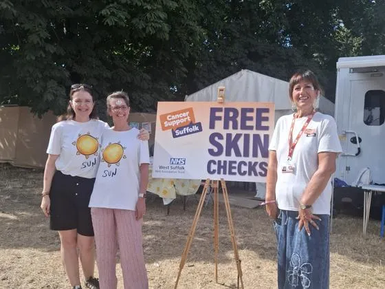 three skin cancer nurses in white shirts stand next to a sign that says 'free skin checks'